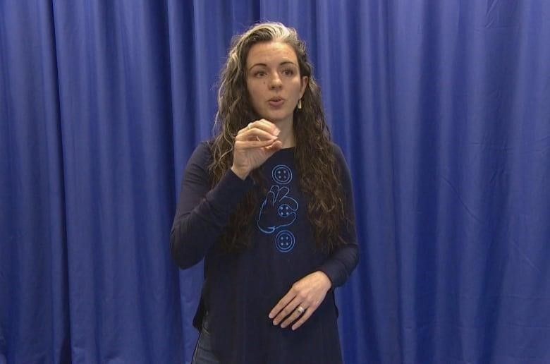 A woman in a dark blue top signs against blue curtains.