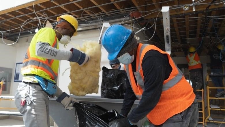 A man holds a piece of insulation as another man packs more into a garbage bag.