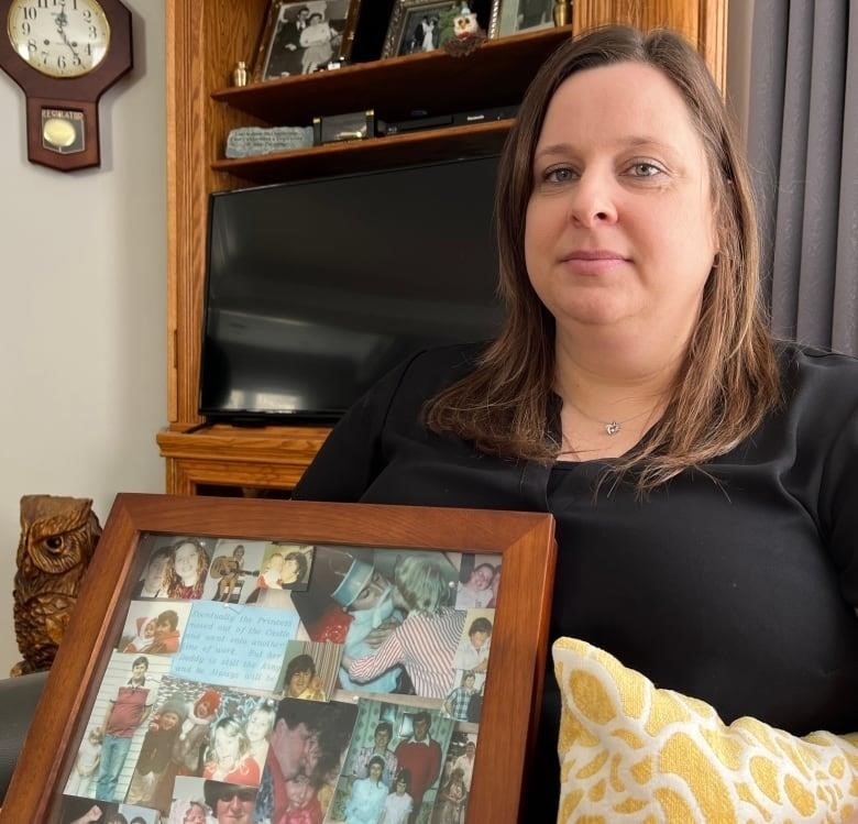 A middle-aged woman looks into the camera. She is seated. On her lap, she's holding a picture frame with a collage of different pictures inside. All pictures show herself as child, and her father and mother.