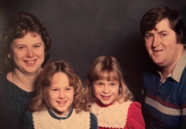 Four people smile — a woman on the left, a man on the right, and two young girls in the centre.