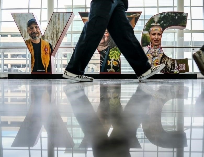 Legs and feet are seen walking in  front of a YYC sign