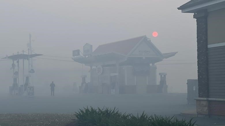 A gas station is shown in a haze of smoke with a red sun in the background.