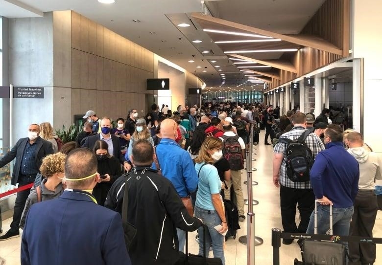 A long line up of people stand in a hallway of an airport