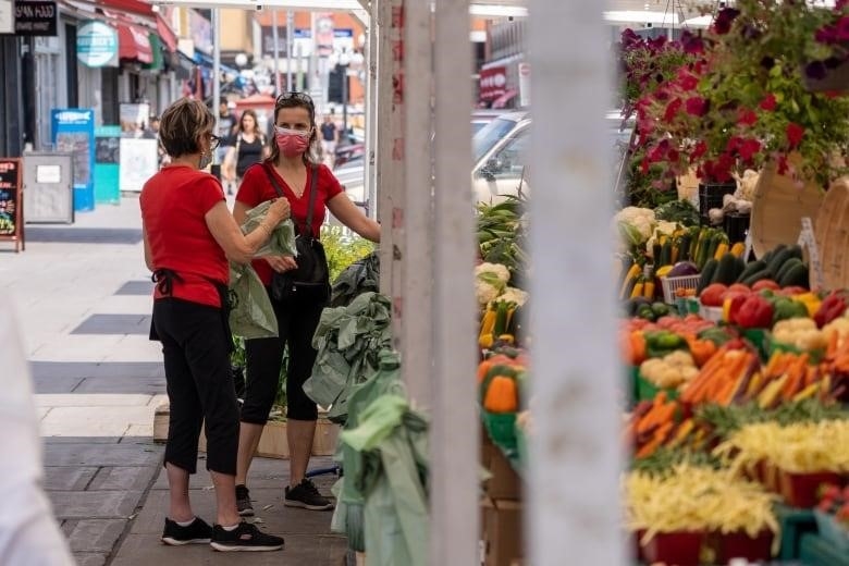 Woman in an apron at an outdoor produce stall speaks with a customer