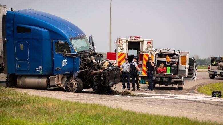 First responders stand near a semi-trailer truck that has been in an accident.