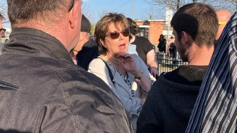 A woman in sunglasses, surrounded by men.