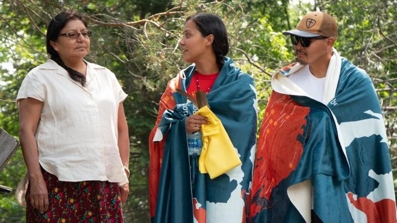 A couple is wrapped in blankets gifted from NAN while standing beside Anna Betty Achneepineskum. 