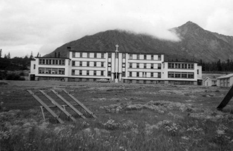 A black and white photo of a large school building with a mountain behind it.