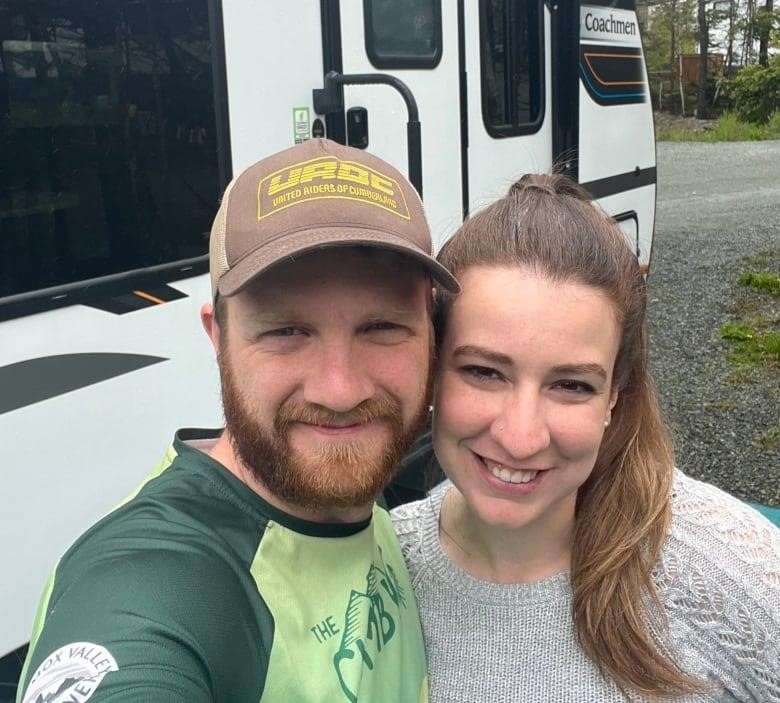 A man and a woman smile for a selfie standing in front of an RV.