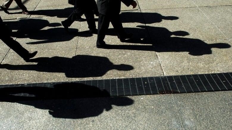 Shadows of men in suits are seen against the pavement. 