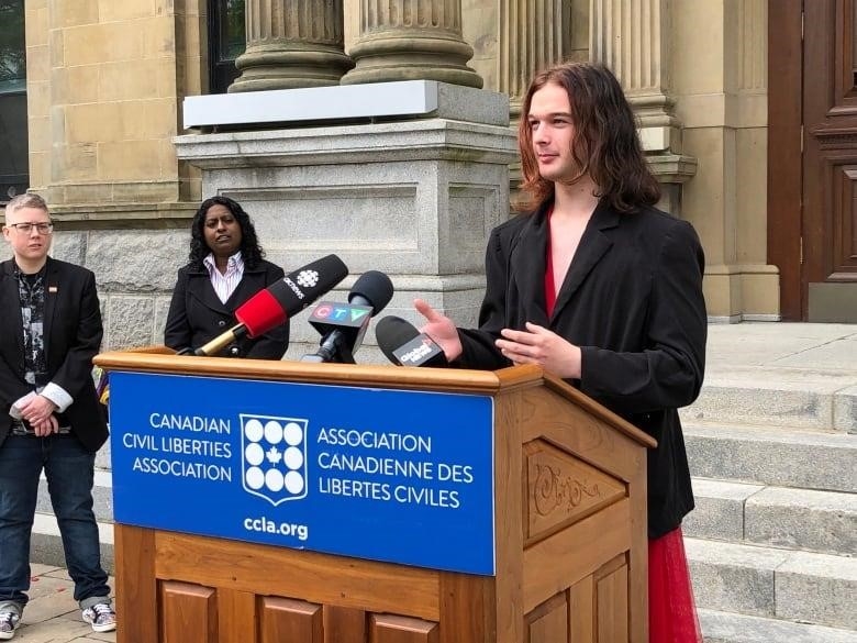 Woman in a red dress, black blazer speaking at podium