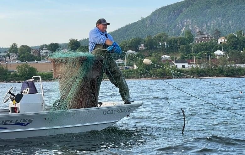 A man standing on the edge of a boat pulling at a net submerged in the water