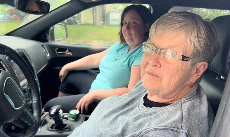 Woman with white hair sits behind the wheel of a car. Another younger woman sits beside her.