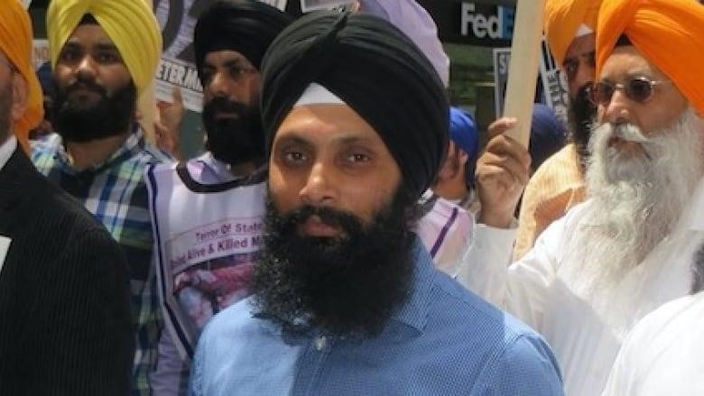A man carries a sign that says "Sikhs Want Their Independence" wearing a blue collared shirt and black turban, surrounded by other men.