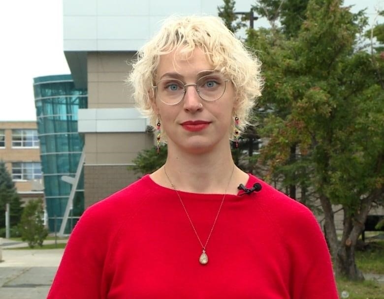 A blonde person wearing red lipstick and a red blouse poses for a picture.