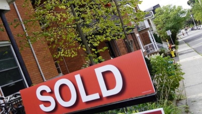 A "sold" sign along a street of townhouses. 