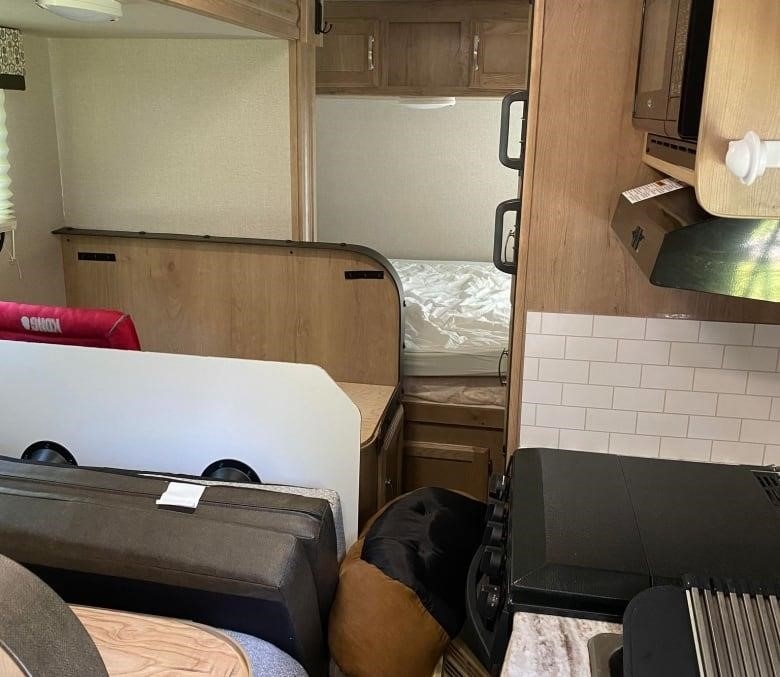 A photograph of the inside of a cramped RV, with a bed, table and stove.