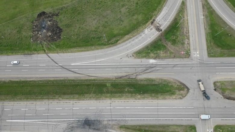 An overhead view of a highway intersection. Several vehicles are on the road, and there are large skid and burn marks across the highway.