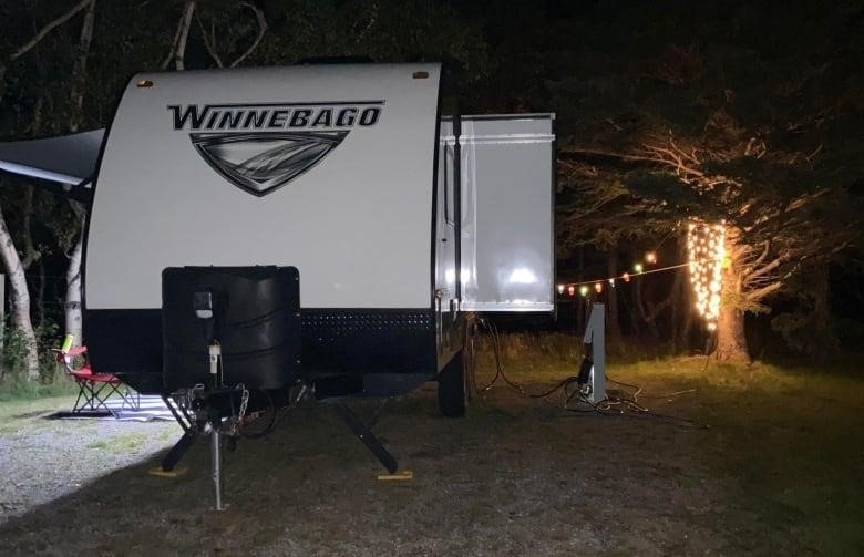 An RV sits outside beside a tree lit up with LED lights under the night sky.