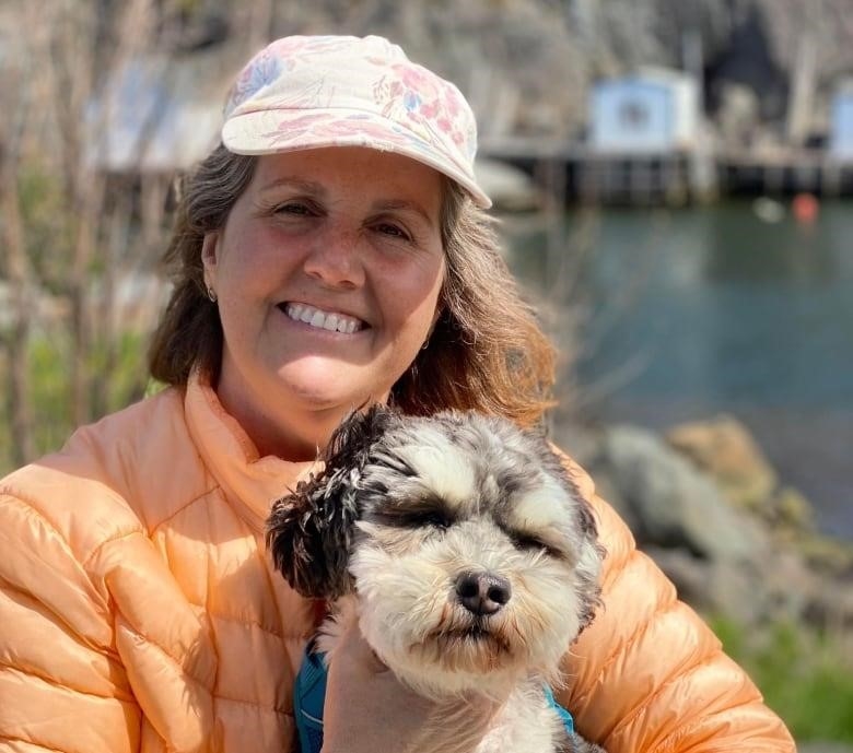 A woman wearing an orange jacket smiles for a photograph while holding her dog.