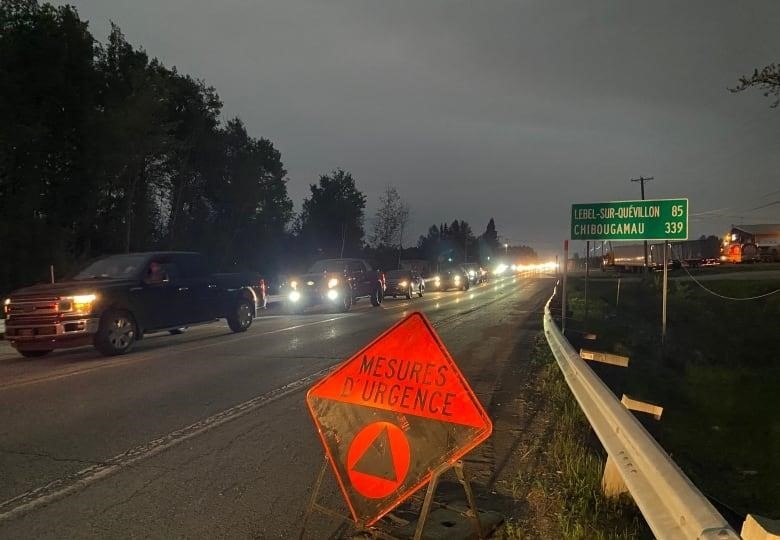 A line of cars on a highway is seen with an orange sign that says "Emergency measures" on the side of the road.