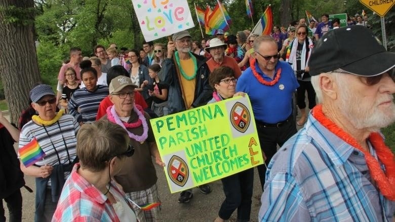 People walk in a Pride parade while carrying signs. 