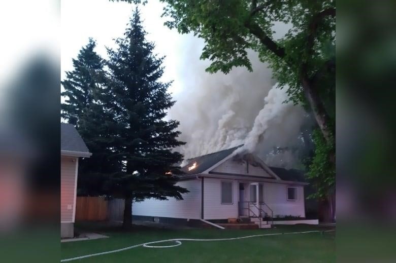 White bungalow house with thick gray smoke coming out of roof.