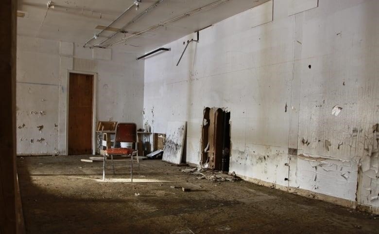 An empty room has a single chair. The walls are beaten up and the floor is dirty. 