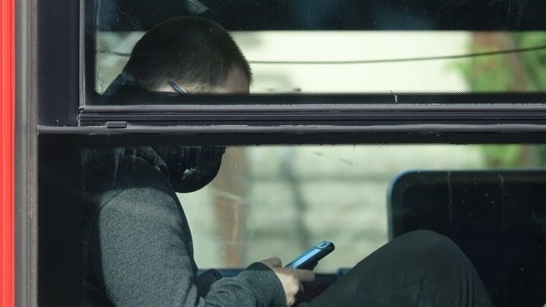 A bus rider wearing a mask checks their phone.