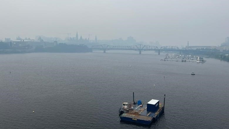 Smoke hangs over the skyline of two cities and the river between them.