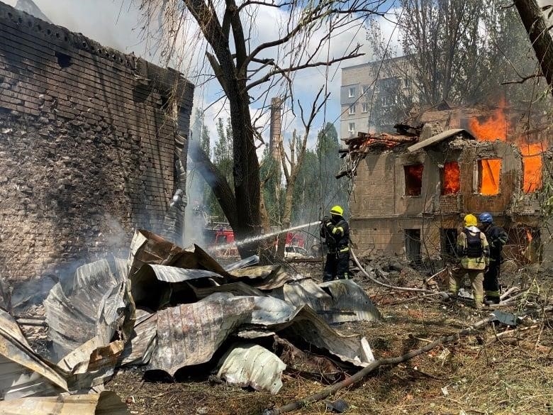 A firefighter sprays water on the ground amid wreckage in front of a destroyed building.