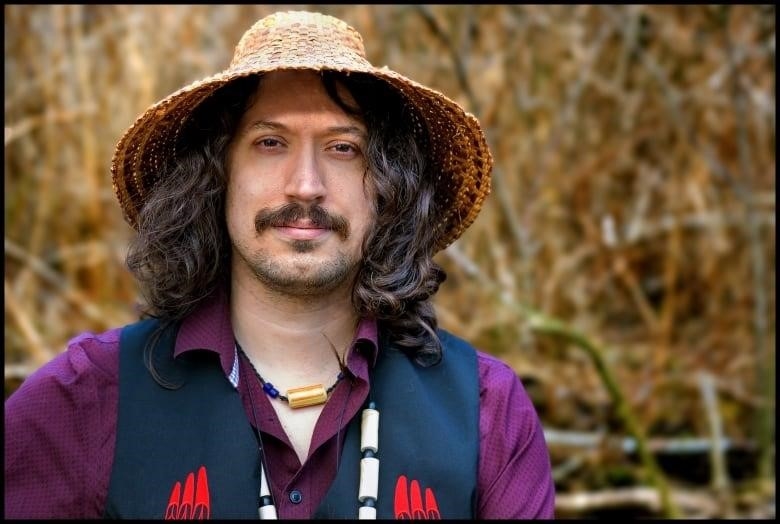 Man stands in a cedar hat outside