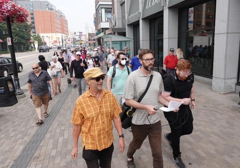 Shawn Menard leads a a group people walking along Bank Street in front of Lansdowne Park