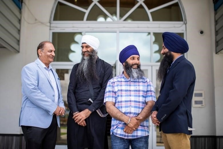 A group of Sikh men speak informally to each other for a posed photograph.