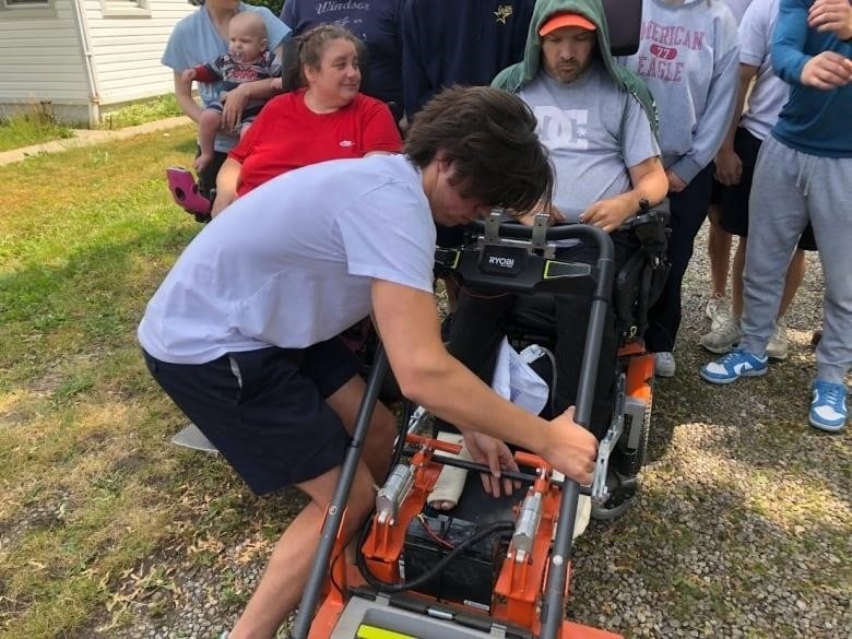 A St. Anne High School student assists Rob Piper as he prepares to mow his Windsor, Ont., lawn.