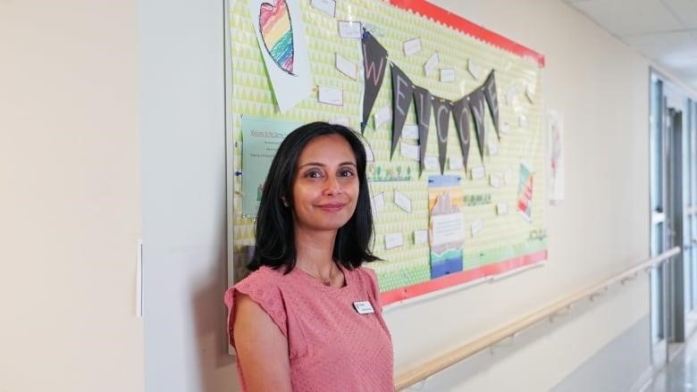  A woman in a pink shirt smiles leaning against a information board.