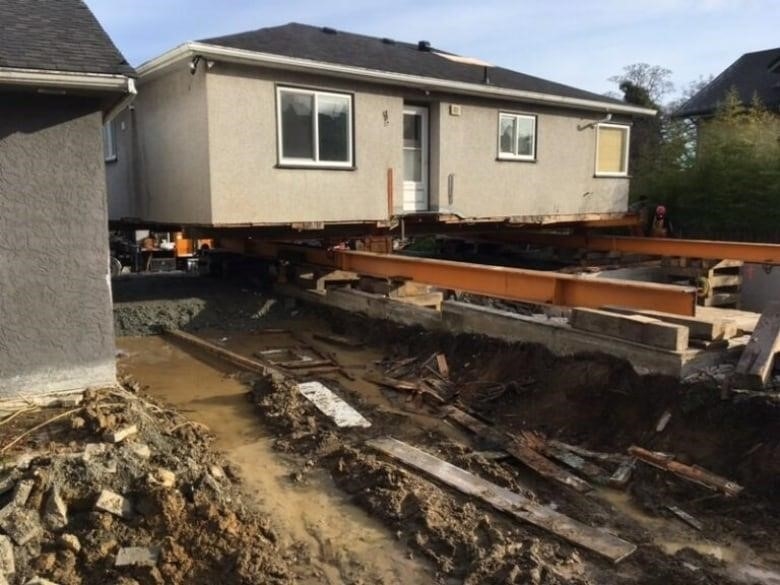 A single-family home sits on lifts above its foundation at a muddy construction site.