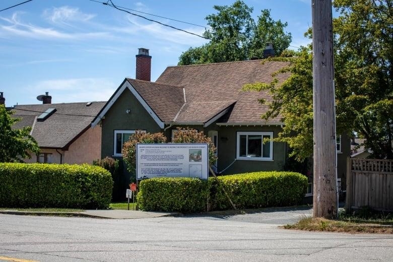 A house is pictured in the daytime, surrounded by shrubs.