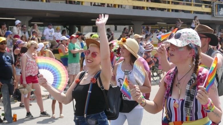 A woman is walking among a crowd of people holding a rainbow coloured fan and waving.