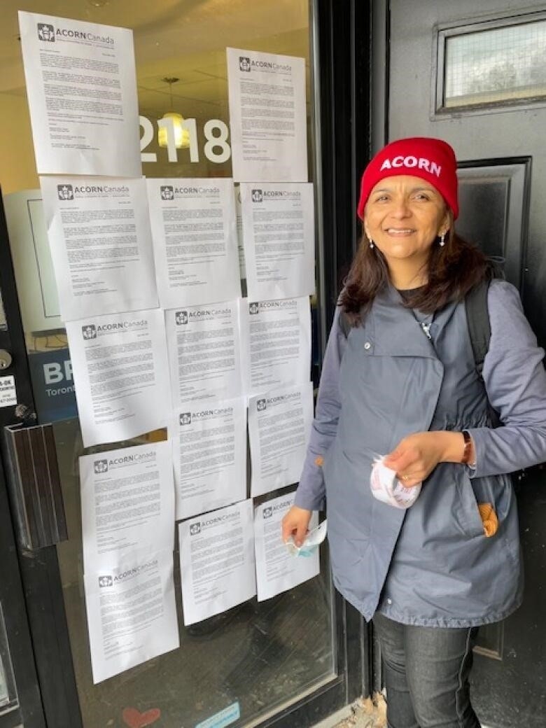 A woman smiles while she stands next to a door with multiple white papers on it. 