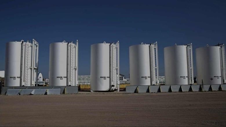 A row of refinery towers. The towers are white before a clear blue sky.