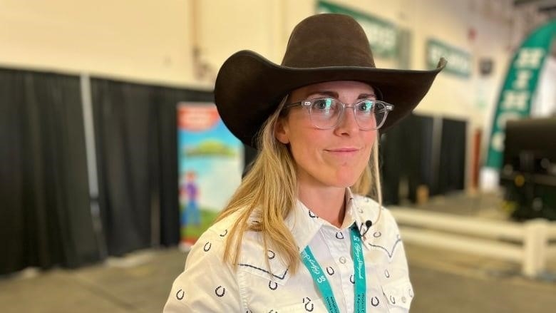 A woman in a cowboy hat and white button down poses for a picture at the Calgary Stampede.