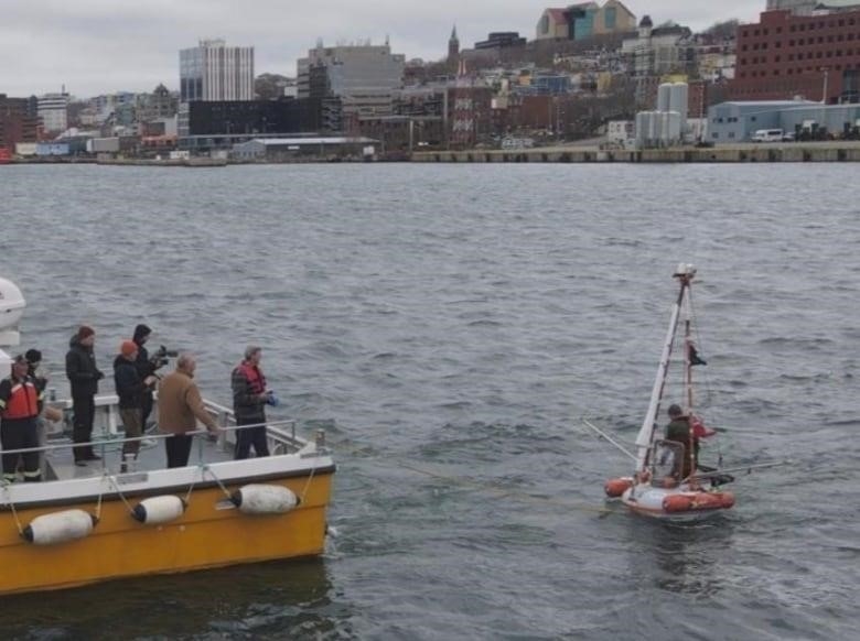 A man in a small boat floats beside a number of people on the deck of a larger boat.