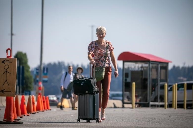 A woman with white hair rolls a suitcase near a B.C. Ferries terminal.