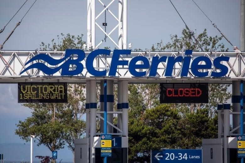 A sign reading 'B.C. Ferries' atop a parking booth, with two signs below it indicating certain lanes are open and closed.