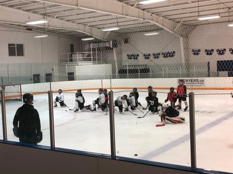 A group of minor hockey players kneel on one knee as they listen to a coach.