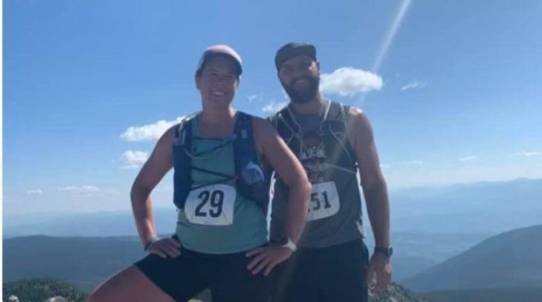 A couple wearing hiking gear, backpacks and bibs with numbers on them are pictured after exercising on a sunny day.