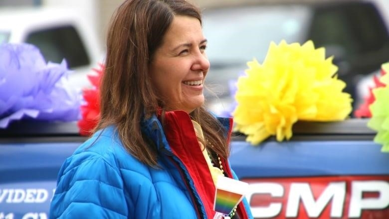woman holds a rainbow noisemaker behind a car dealership's Pride parade float