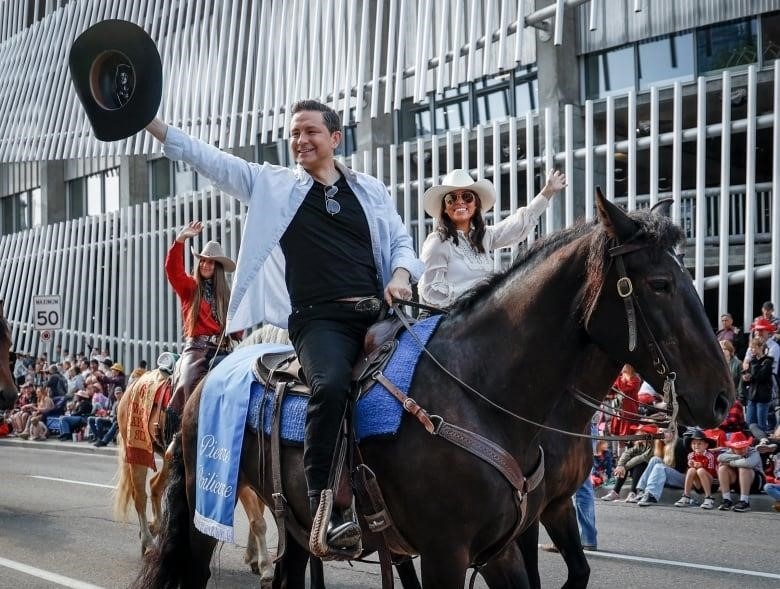 A man riding a horse holding a black cowboy hat waving to the crowd.