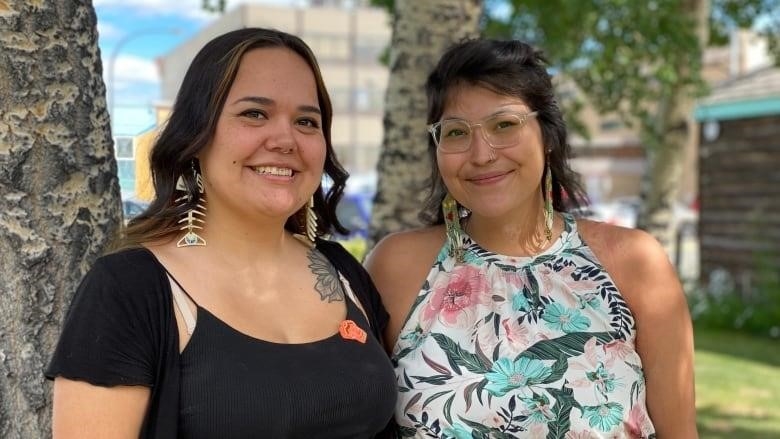 Two smiling young women stand together on a lawn.